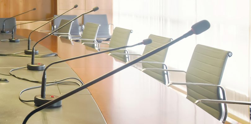 Microphone on a wooden table and empty chairs in a boardroom.