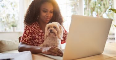 Young woman sitting with her dog and using a laptop
