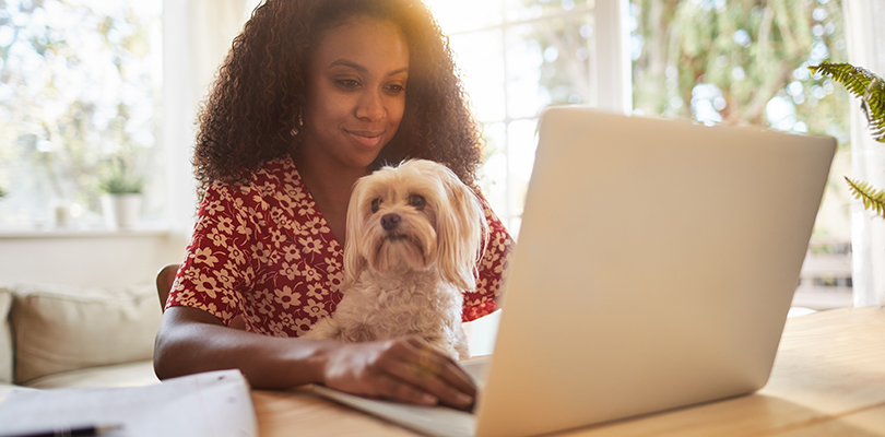 Young woman sitting with her dog and using a laptop