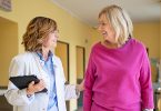 Doctor with senior woman walking in hospital corridor