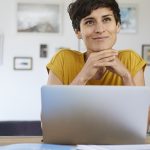 Portrait of smiling woman at home sitting at table using laptop