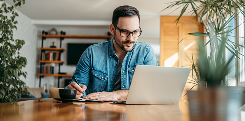 Man taking notes and looking at laptop, at home office, portrait.