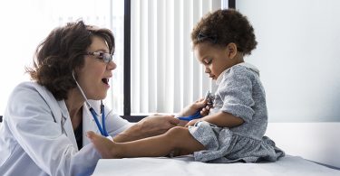 Female doctor examining baby girl with stethoscope