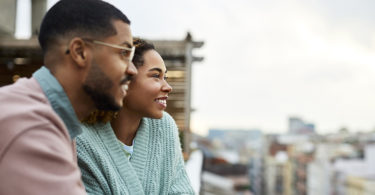 Happy young couple looking away while holding hands at rooftop. Smiling woman is spending leisure time with boyfriend. They are enjoying at building terrace.