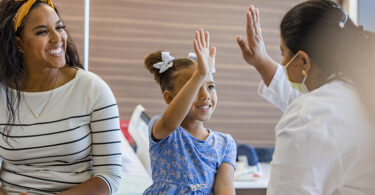 Doctor giving a child a high-five but still wearing a mask because of COVID-19