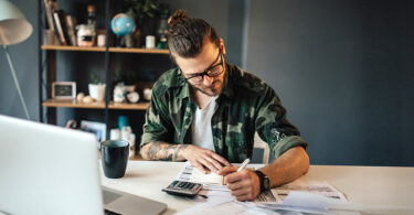 Tattooed hipster is using a calculator to sum all the bills