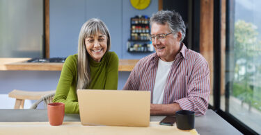 Smiling mature couple using a laptop together at a table at home