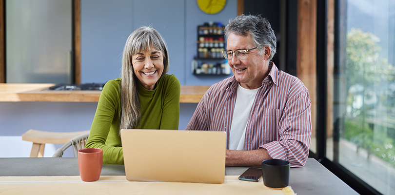 Smiling mature couple using a laptop together at a table at home
