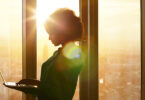 Businesswoman on laptop at window in morning sun
