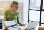 Woman entering information into a laptop computer holding a piece of paper in right hand