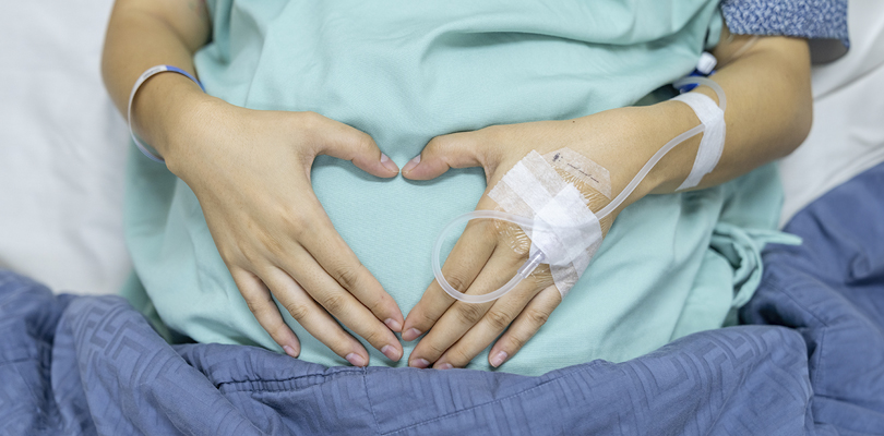 Pregnant person making a heart with their hands over their stomach