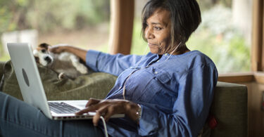 Middle-aged black woman using laptop computer and petting dog