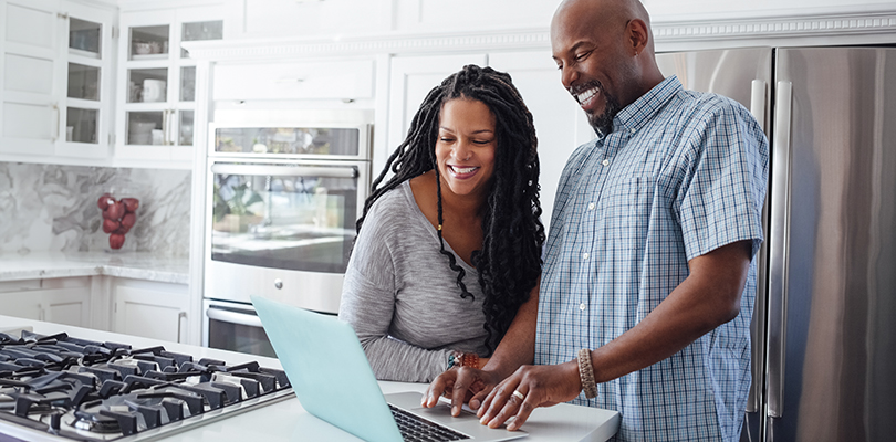 Man and woman using laptop in kitchen at home