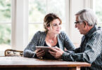 Young woman holding tablet talking to older man.