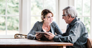 Young woman holding tablet talking to older man.