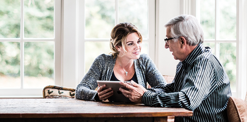 Young woman holding tablet talking to older man.