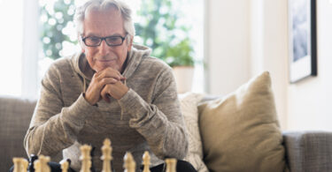 Older man sitting on sofa looking at chess board