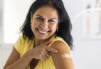 Smiling woman pointing to a small bandage on her upper arm