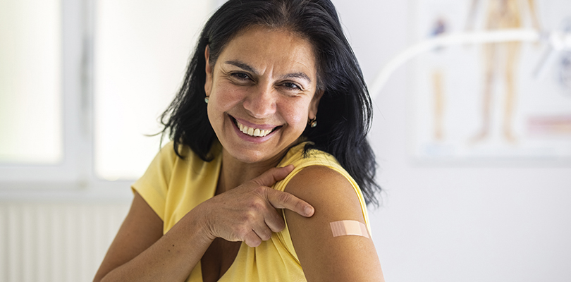 Smiling woman pointing to a small bandage on her upper arm