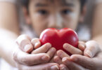 Offscreen parent and child both holding a heart towards the camera