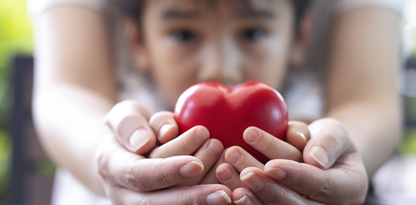 Offscreen parent and child both holding a heart towards the camera