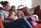 Same sex couple enjoying a cuddle together at home, with their baby daughter and their pet dog.