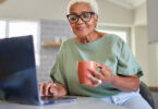 Senior Black woman holding mug in one hand using laptop with the other