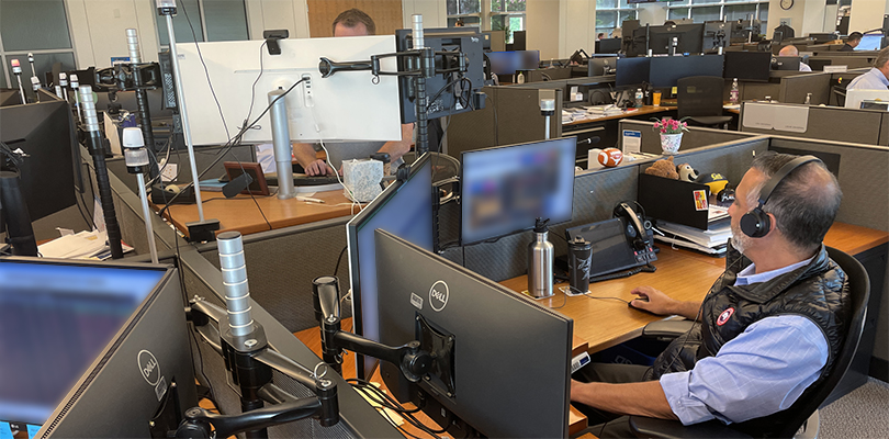 Man sitting at desk with three monitors, monitor screen blurred as to protect sensitive data/information