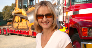 Heather Huerta smiling in front of 18-wheeler hauling a bulldozer