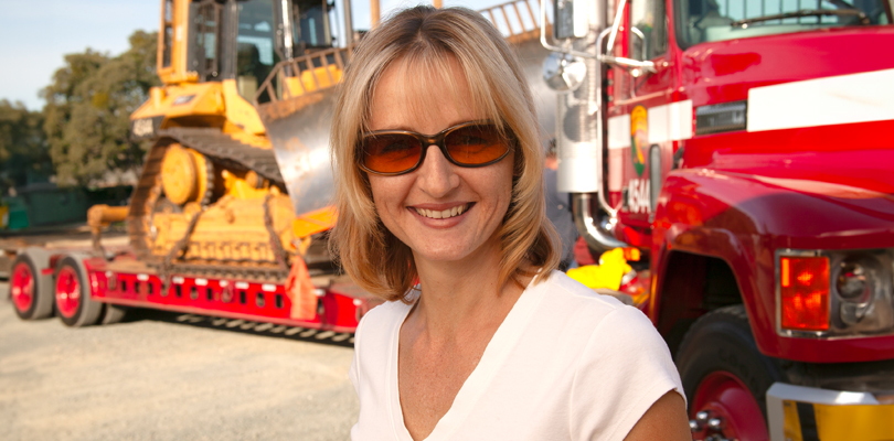 Heather Huerta smiling in front of 18-wheeler hauling a bulldozer