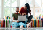 Man sitting down using laptop with wife next to him