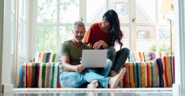 Man sitting down using laptop with wife next to him