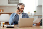 Older man on phone sitting in front of table with laptop