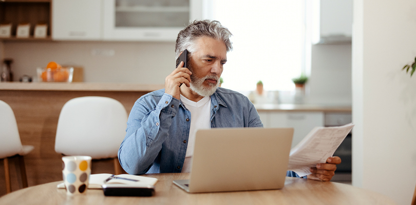 Older man on phone sitting in front of table with laptop