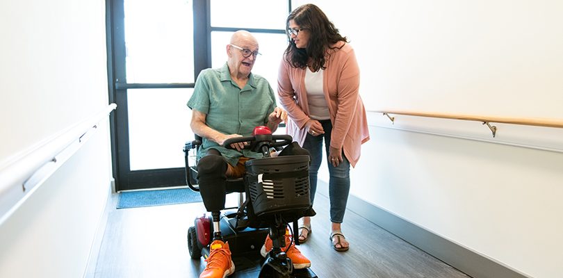 Man using motorized wheelchair talking to woman
