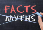 Off-screen person writing the words "Facts" and "Myths" using chalk on a chalkboard with the word "Myths" crossed out.