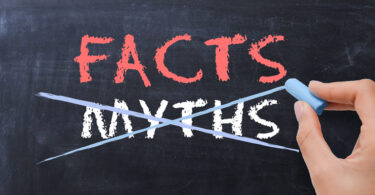 Off-screen person writing the words "Facts" and "Myths" using chalk on a chalkboard with the word "Myths" crossed out.